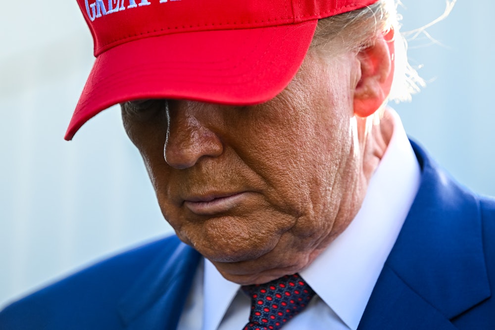 Donald Trump in his red MAGA hat looking down