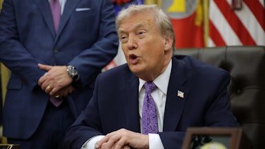 Donald Trump speaks while seated at his desk in the Oval Office of the White House. He places his left hand on his right one, which has the bruise.