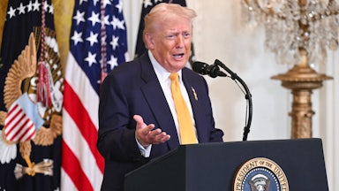 Donald Trump gestures with one hand speaks at a podium