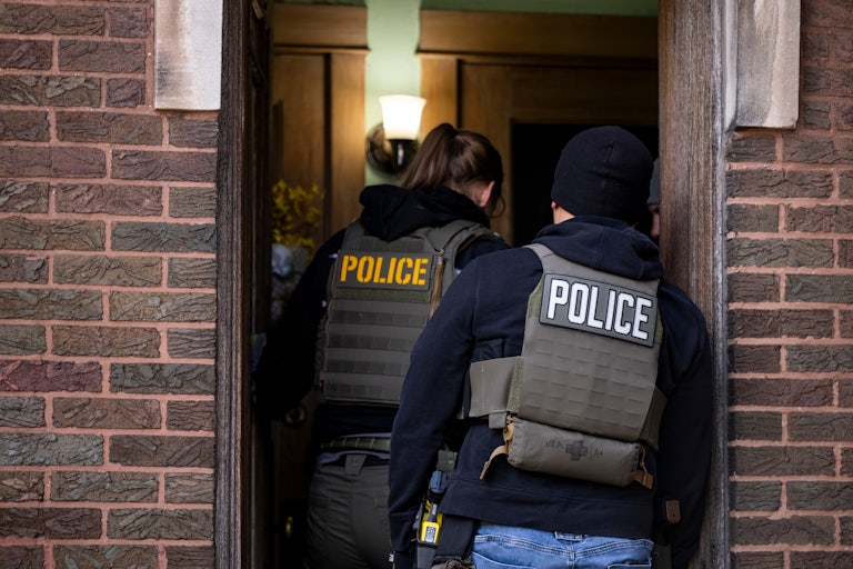Two people wearing POLICE vests walk in through a door.