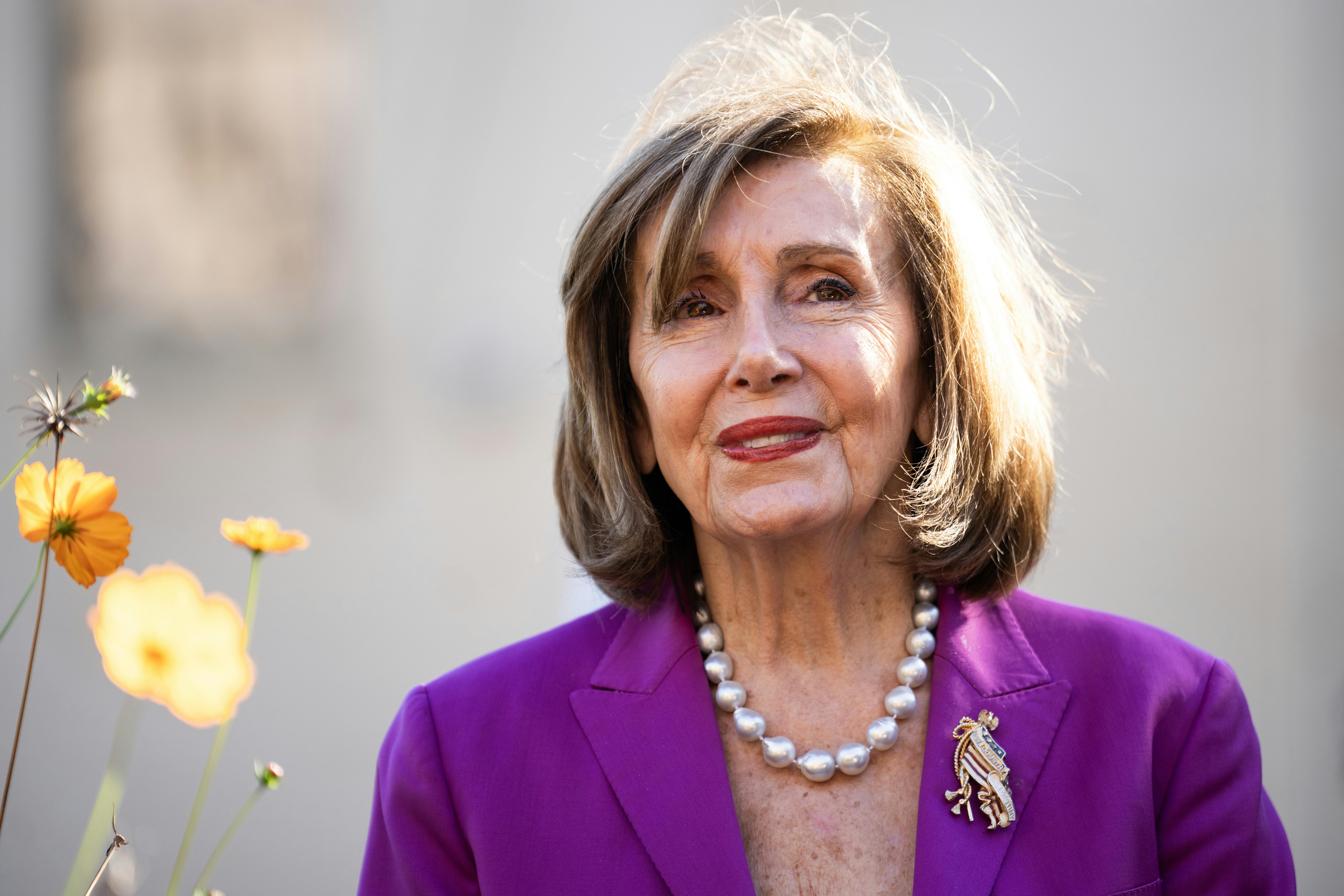 Former House Speaker Nancy Pelosi smiles while standing outside at an event