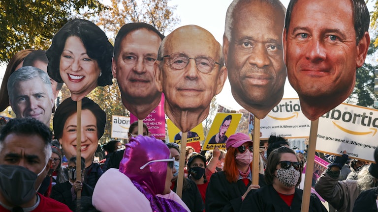 Protesters hold up giant depictions of the Supreme Court Justices’ heads outside the Supreme Court building.