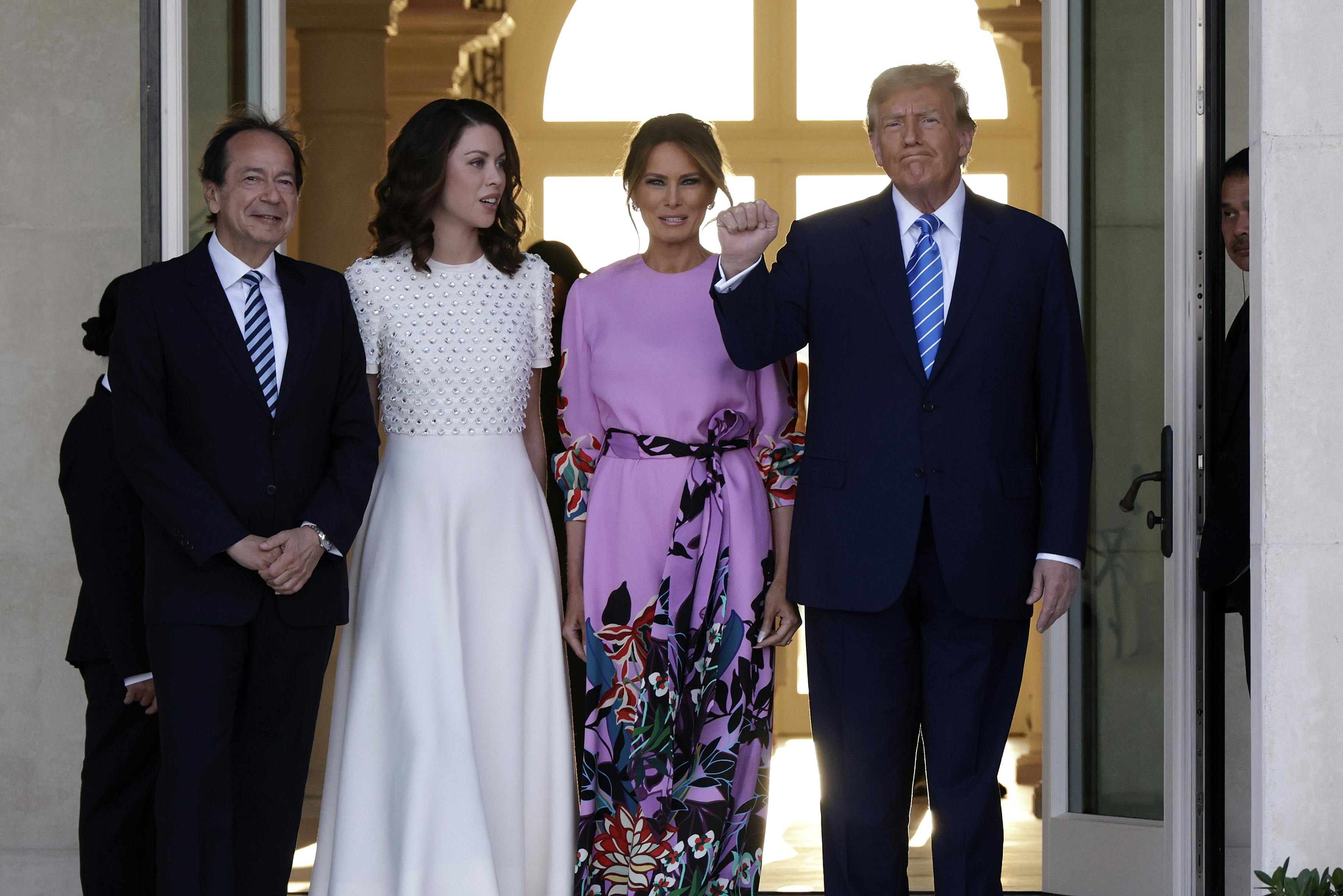 John Paulson, Alina de Almeida, Melania Trump, and Donald Trump smile and pose for photo in front of a pair of large open doors..