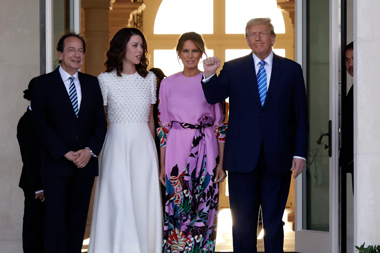 John Paulson, Alina de Almeida, Melania Trump, and Donald Trump smile and pose for photo in front of a pair of large open doors..
