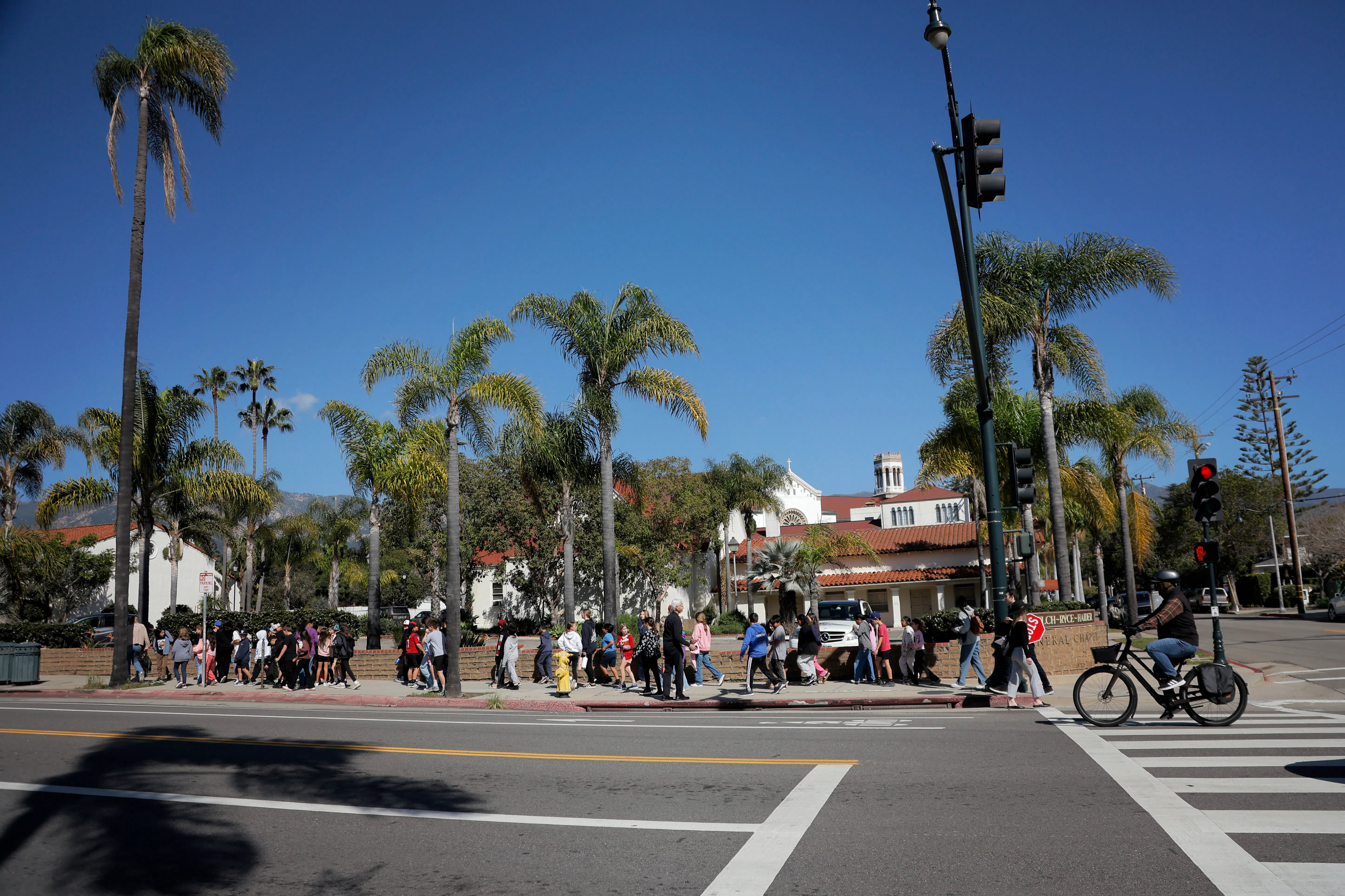 A view of a Santa Barbara California city street, with people walking on a sidewalk in front of palm treets and buildings.