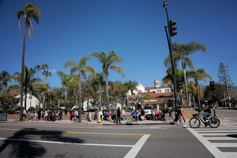 A view of a Santa Barbara California city street, with people walking on a sidewalk in front of palm treets and buildings.