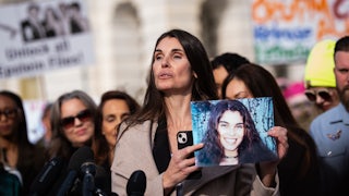 An Epstein survivor holds a picture of herself up in a press conference outside the Capitol. Others gather behind her.