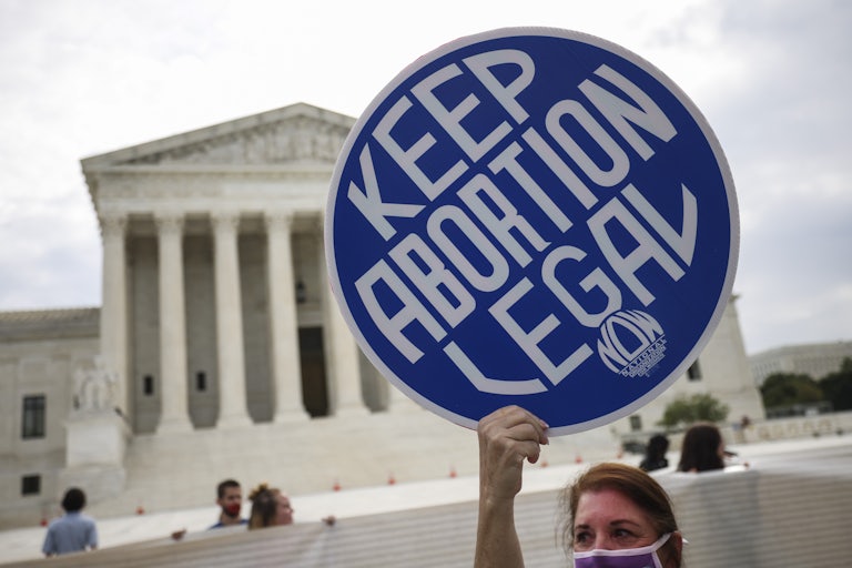 A woman holds a sign reading "Keep Abortion Legal" on the sidewalk in front of the Supreme Court.