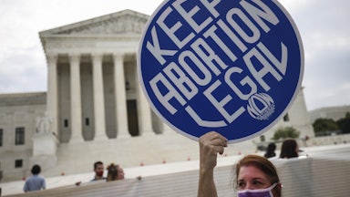 A woman holds a sign reading "Keep Abortion Legal" on the sidewalk in front of the Supreme Court.