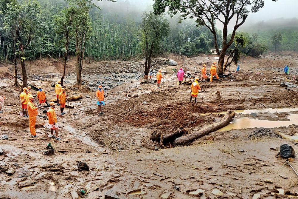 People in orange gear walk on mud, looking for survivors.