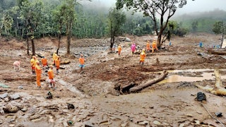 People in orange gear walk on mud, looking for survivors.