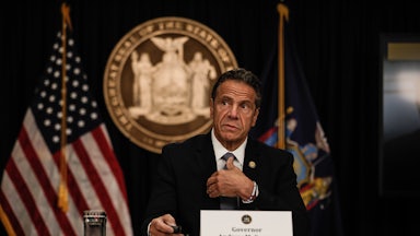 New York Governor Andrew Cuomo speaks at a news conference with flags and a state seal behind him.