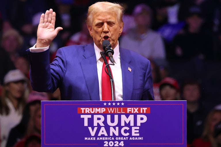 Donald Trump raises his hand as if pledging something, while speaking behind a lectern at his Madison Square Garden rally