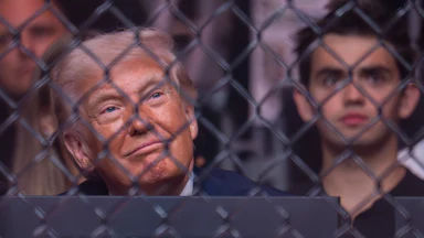 Donald Trump smiles and looks up while seated in the audience of a UFC match