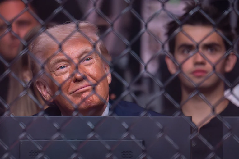 Donald Trump smiles and looks up while seated in the audience of a UFC match