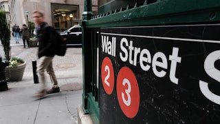 An image of the Wall Street subway entrance in New York, with a blurry figure walking past it.