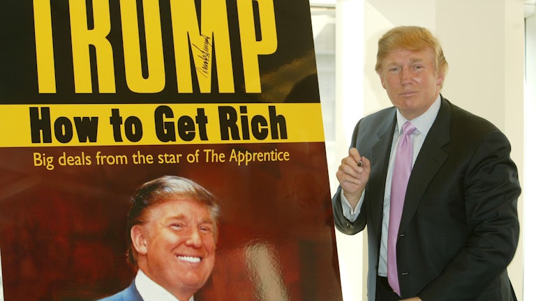 Donald Trump stands in front of a poster advertising one of his books.