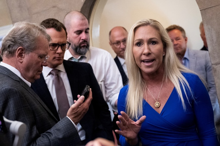 Marjorie Taylor Greene yells and holds up a hand as if to say Stop. Reporters surround her.