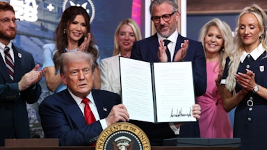 Donald Trump holds up a signed order as others, including Homeland Security Secretary Kristi Noem, clap behind him.