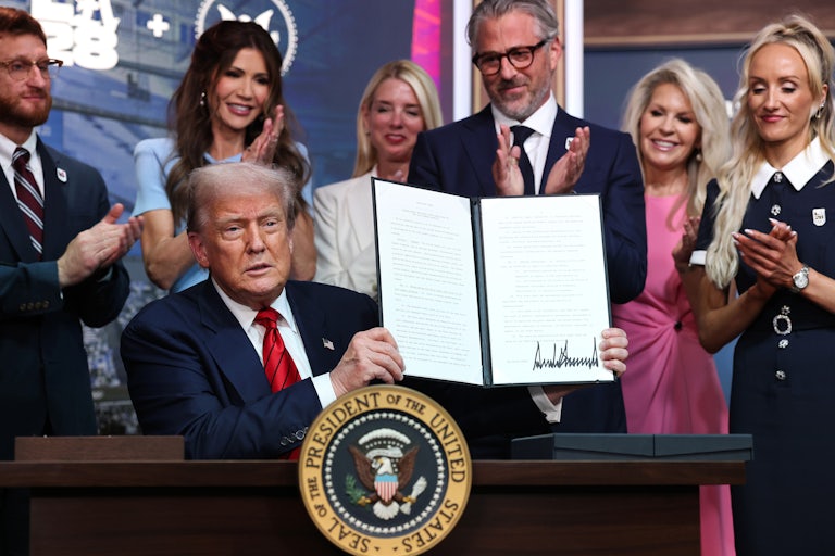 Donald Trump holds up a signed order as others, including Homeland Security Secretary Kristi Noem, clap behind him.