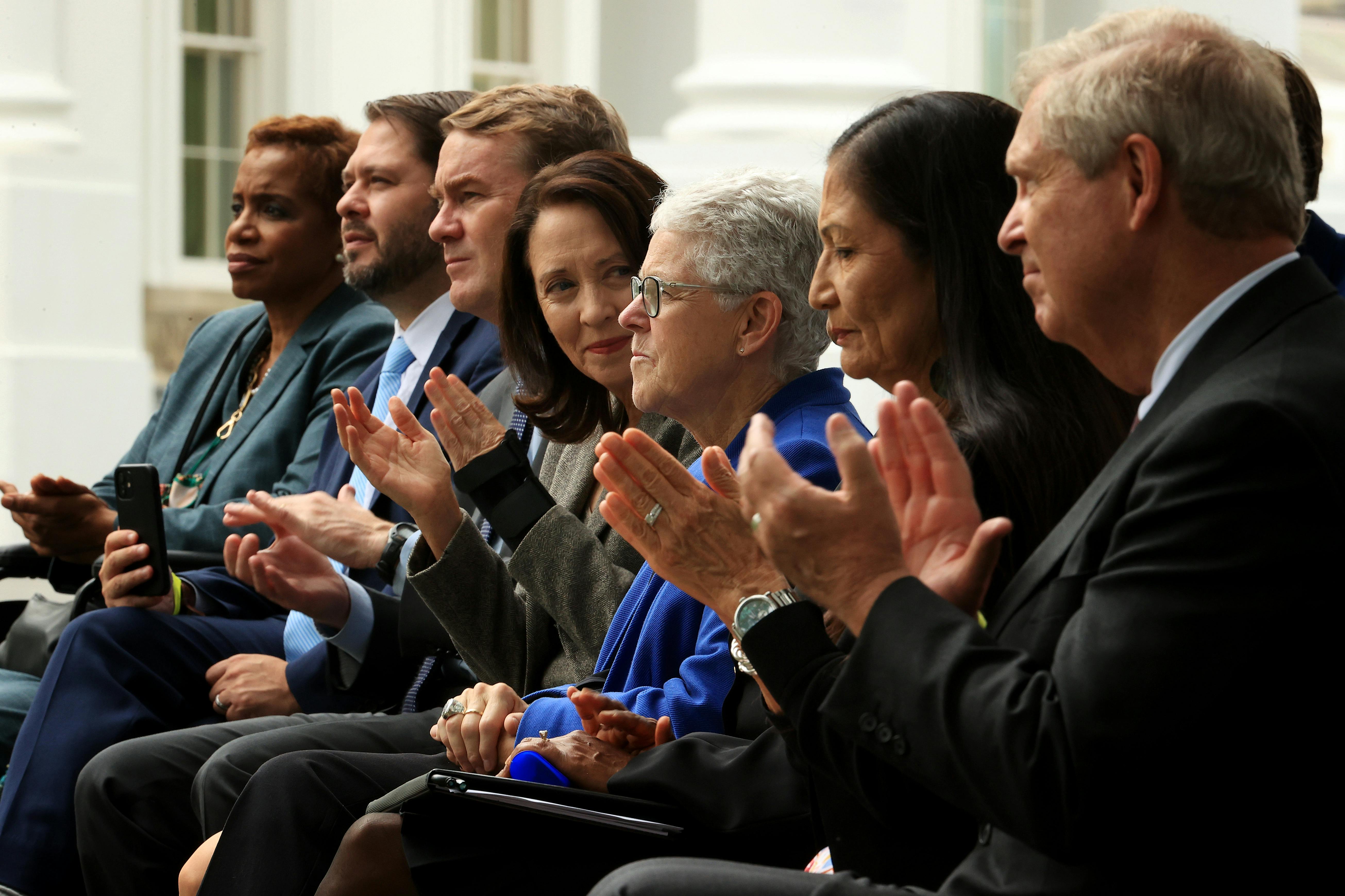 Gina McCarthy sits surrounding by people clapping. She clasps her hands.