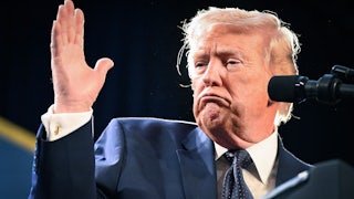 Donald Trump making a weird face and a hand gesture while speaking at a podium.