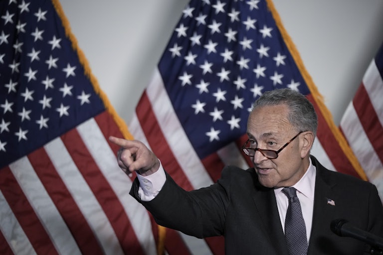 Chuck Schumer stands in front of American flags, pointing off-camera.