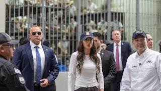 El Salvador’s Minister of Justice and Public Security Héctor Villatoro accompanies U.S. Homeland Security Secretary Kristi Noem stand alongside others, in front of a prison cell holding dozens of men dressed in white.