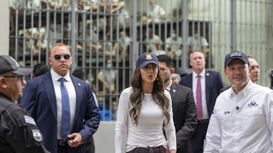 El Salvador’s Minister of Justice and Public Security Héctor Villatoro accompanies U.S. Homeland Security Secretary Kristi Noem stand alongside others, in front of a prison cell holding dozens of men dressed in white.