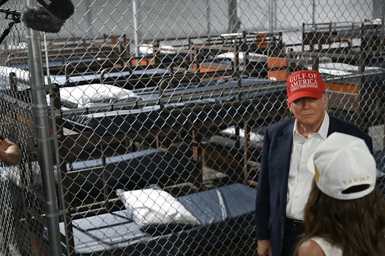 Donald Trump speaks with DHS Secretary Kristi Noem in front of a cage at Florida’s “Alligator Alcatraz” detention facility.
