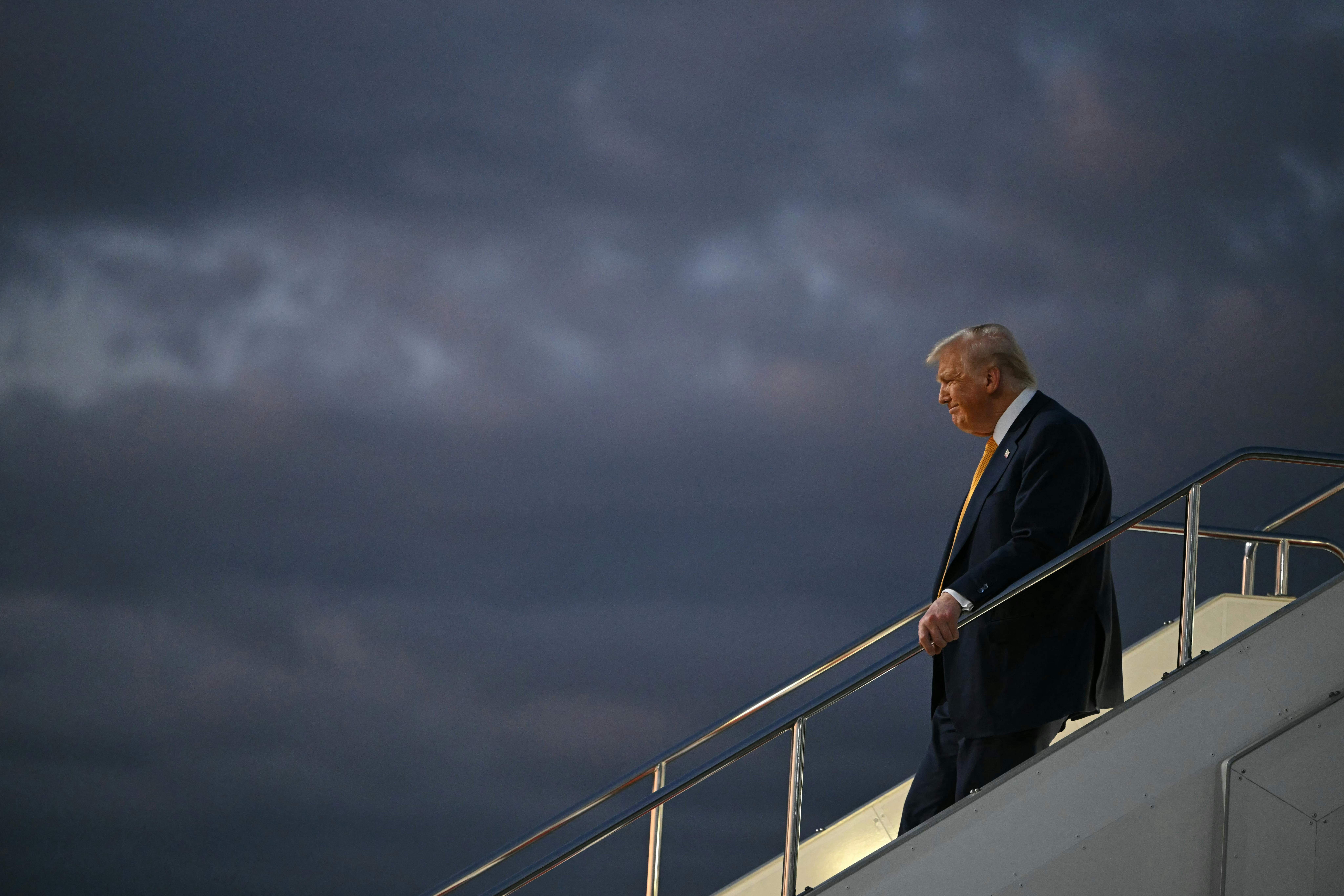 Donald Trump holds the stairs handrail while disembarking from Air Force One