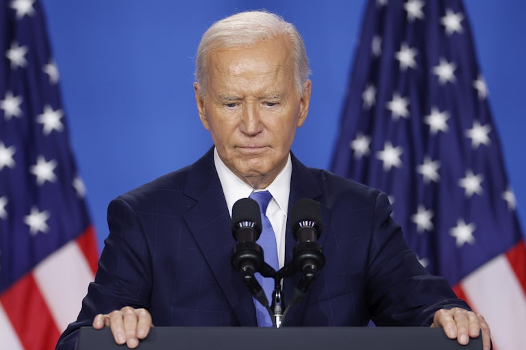Joe Biden looks down while standing at a podium during the NATO summit
