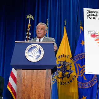 RFK Jr. stands at a podium next to a poster of the new, inverted food pyramid.