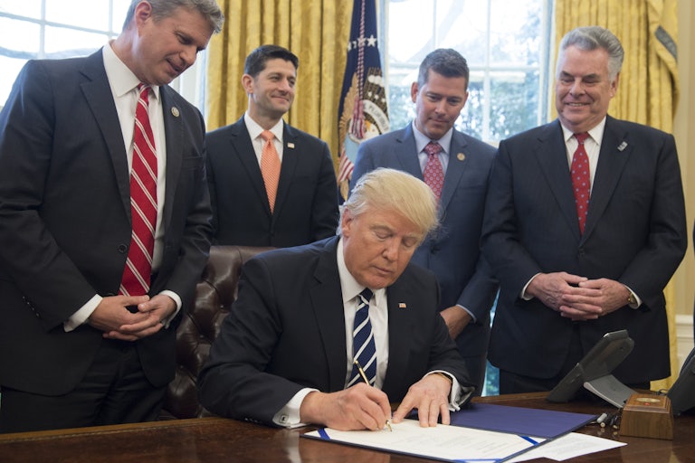 Donald Trump signs a piece of paper at his desk in the Oval Office