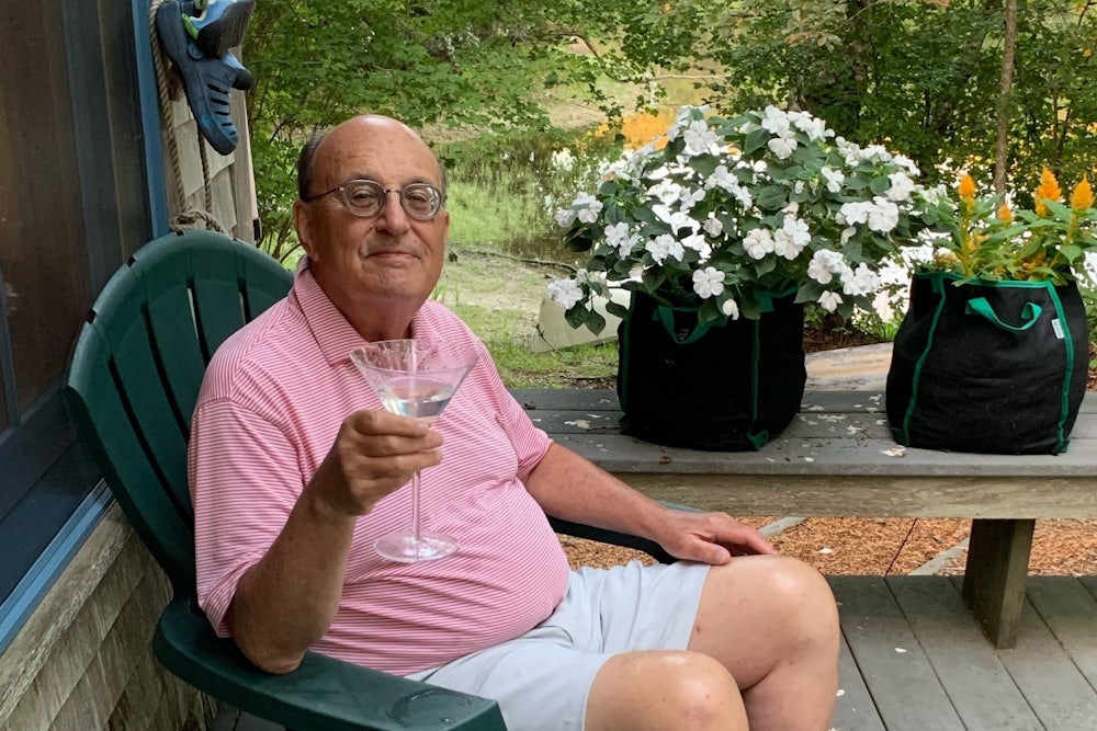 Longtime New Republic staff writer Walter Shapiro holds a martini while sitting in a deck chair.