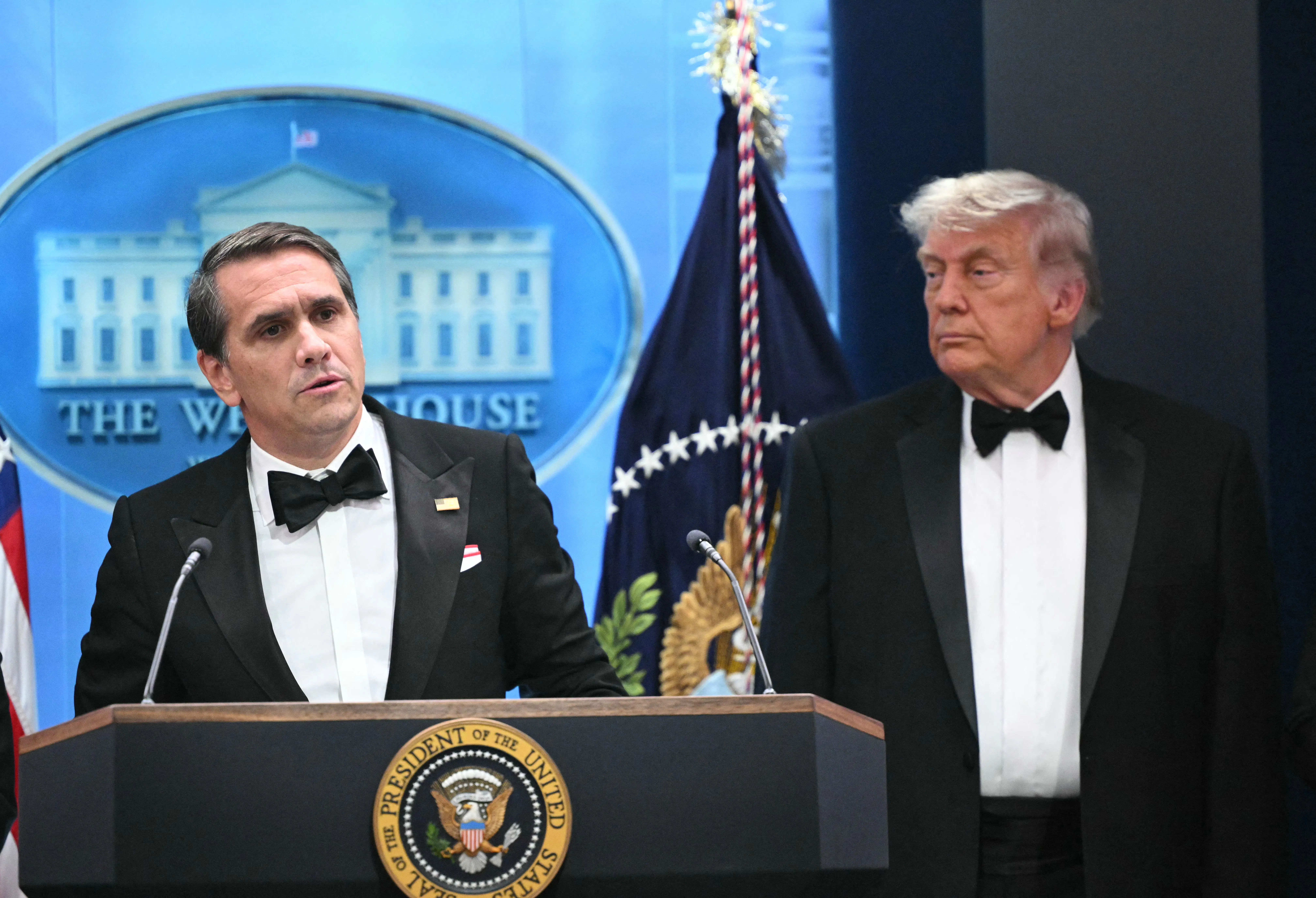 Acting Attorney General Todd Blanche speaks at a podium while Donald Trump stands next to him