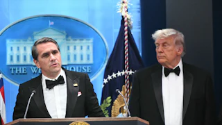 Acting Attorney General Todd Blanche speaks at a podium while Donald Trump stands next to him