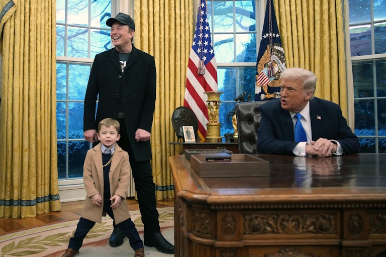 Donald Trump sits at his desk in the Oval Office while Elon Musk and his young son (dressed in a trenchcoat and a gold chain) stand nearby.