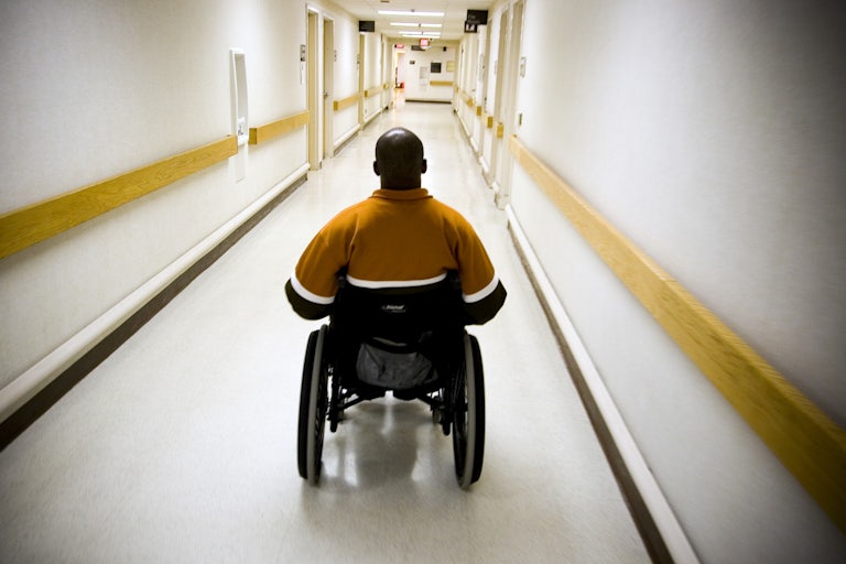 A Black man in a wheelchair goes down a health facility hallway.