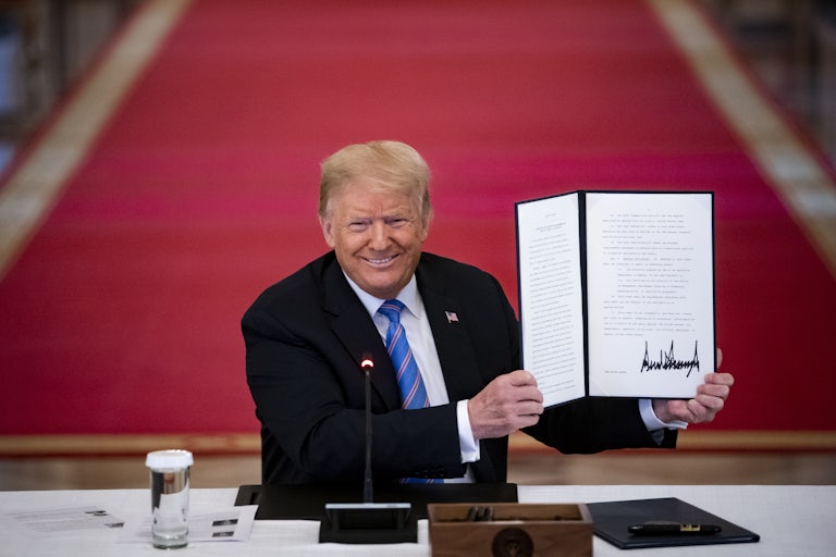 Donald Trump proudly holds up a signed order. A red carpet can be seen behind him.