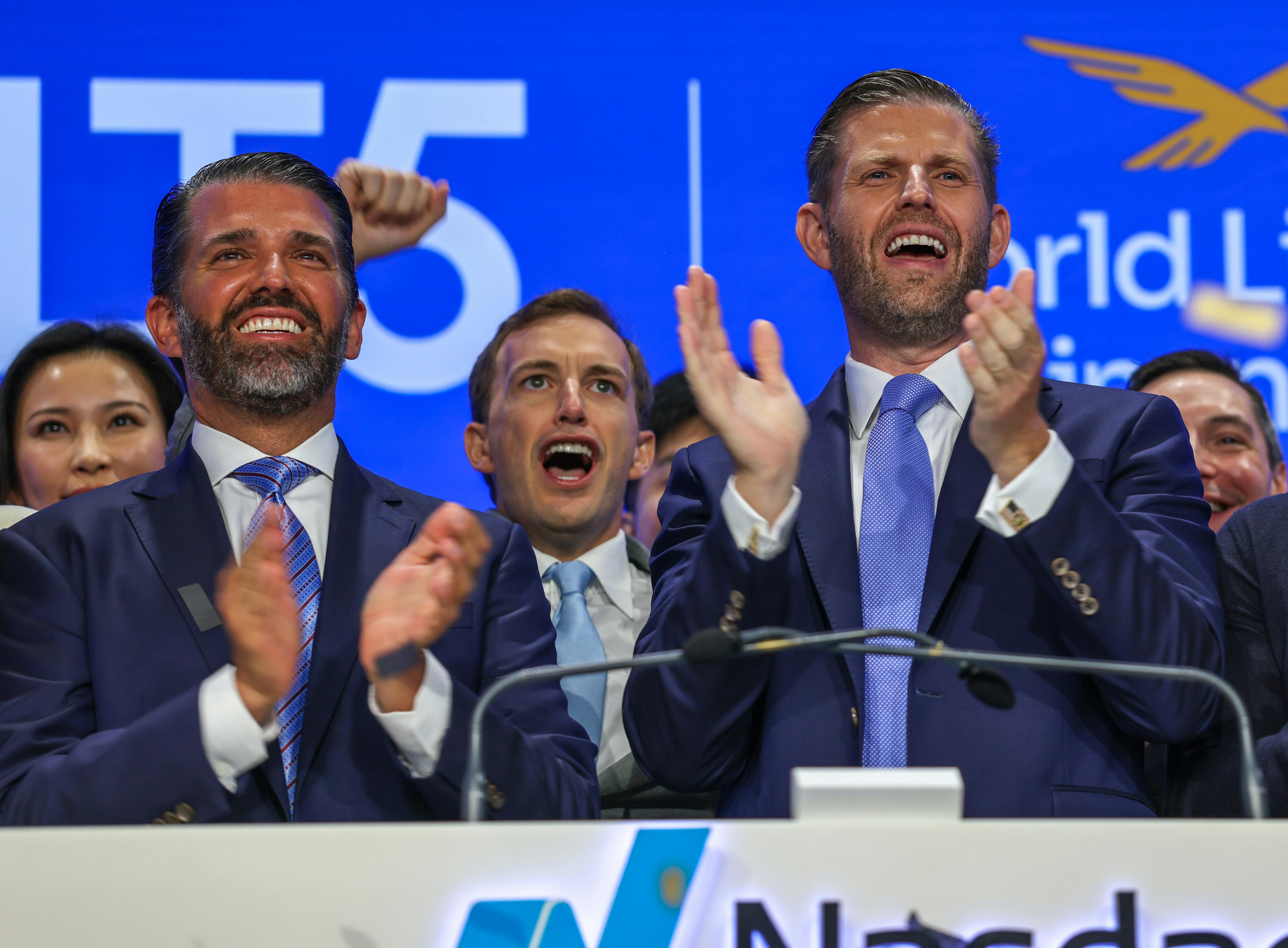 Eric Trump and Donald Trump Jr. clap at NASDAQ while standing in front of Zach Witkoff and a group of other men.