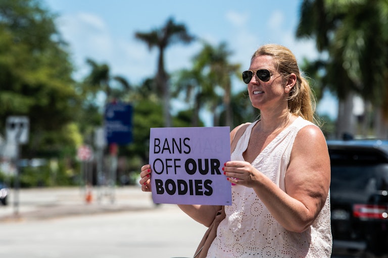 A woman outside holds a sign reading "BANS OFF OUR BODIES"