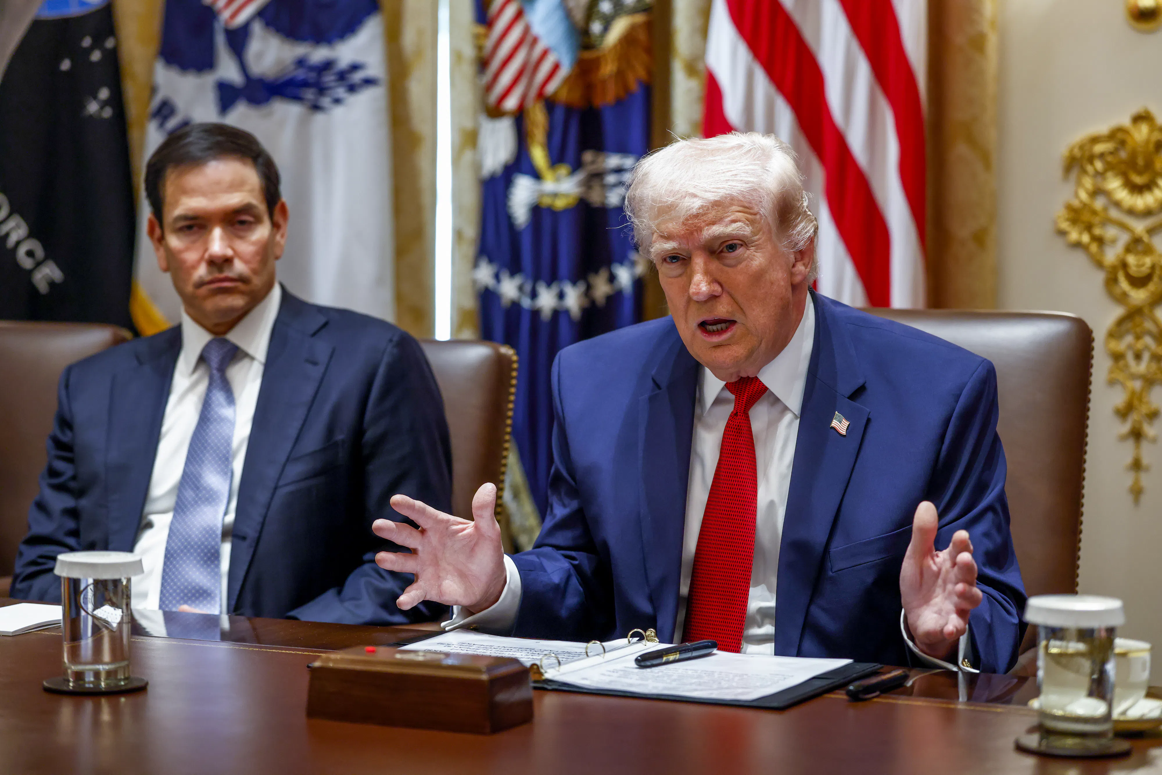 Donald Trump gestures and speaks while sitting next to Secretary of State Marco Rubio at a conference table