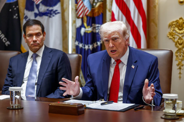 Donald Trump gestures and speaks while sitting next to Secretary of State Marco Rubio at a conference table