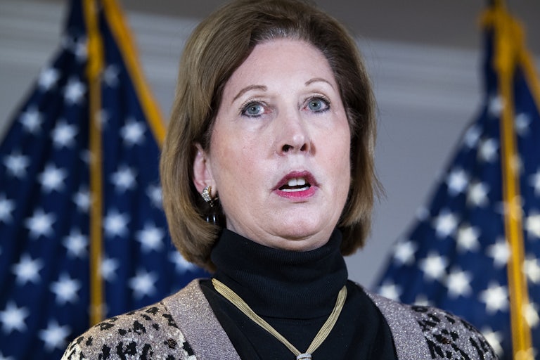 Sidney Powell wears a black turtleneck and a cheetah print cardigan. This is a closeup while she is speaking.
