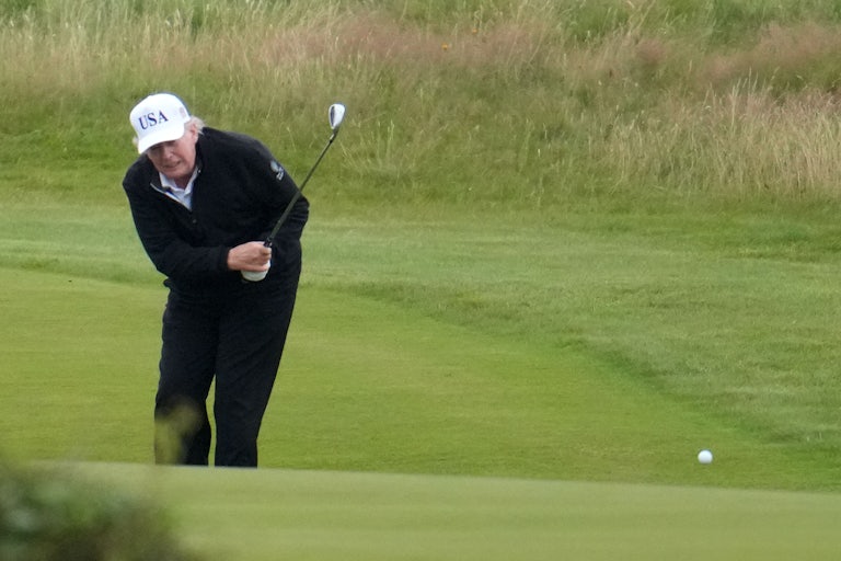 Donald Trump swings a golf club and bends low at the hip.