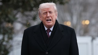 Trump opens his mouth to say something while standing outside in a dark overcoat.