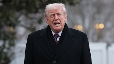 Trump opens his mouth to say something while standing outside in a dark overcoat.