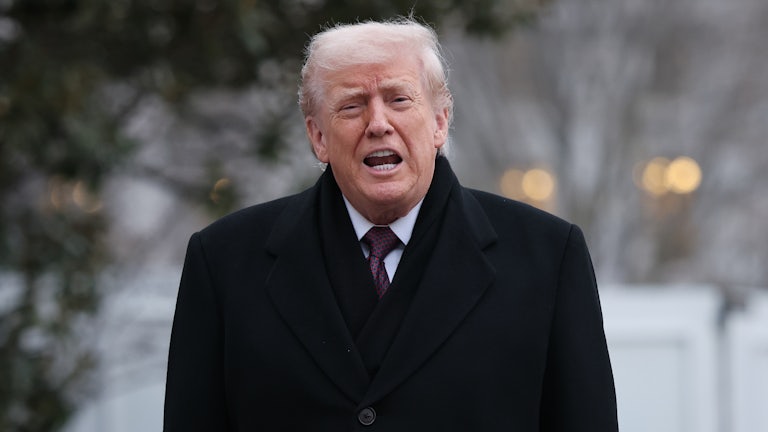 Trump opens his mouth to say something while standing outside in a dark overcoat.