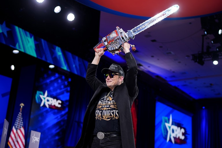 Elon Musk waves a chainsaw over his head while on stage at CPAC
